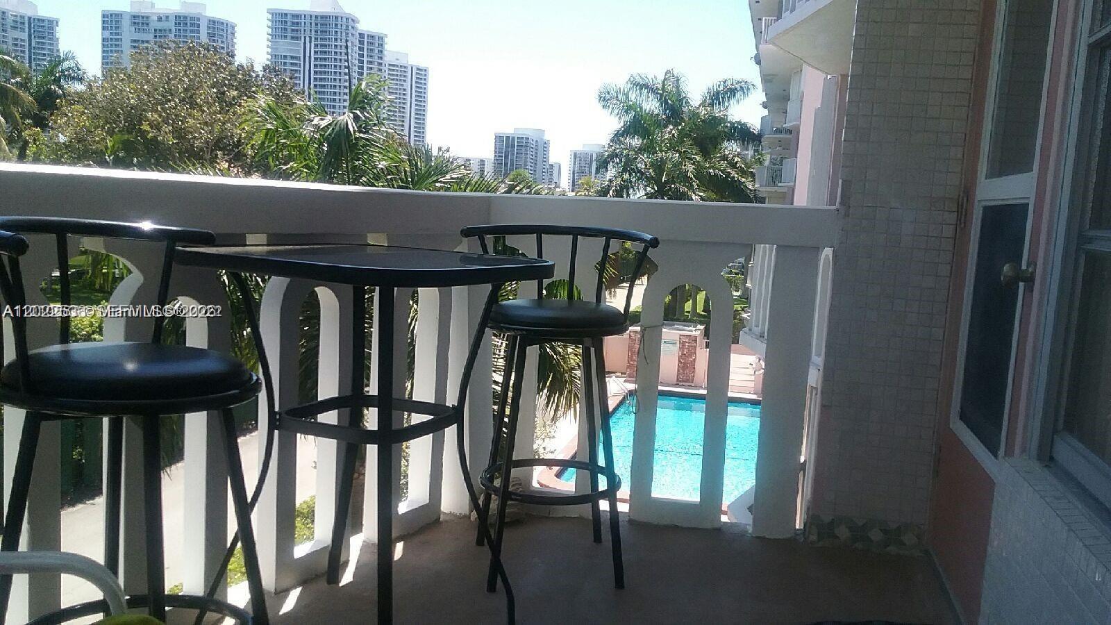 A balcony features a small table with two bar stools overlooking a swimming pool — HALLANDALE BEACH, FL