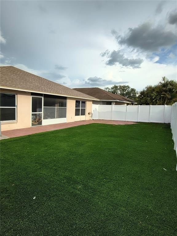 A backyard with artificial turf, a white vinyl fence, and a house with a screened-in patio — 1213 HUMBLE HAVEN STREET, RUSKIN, FL