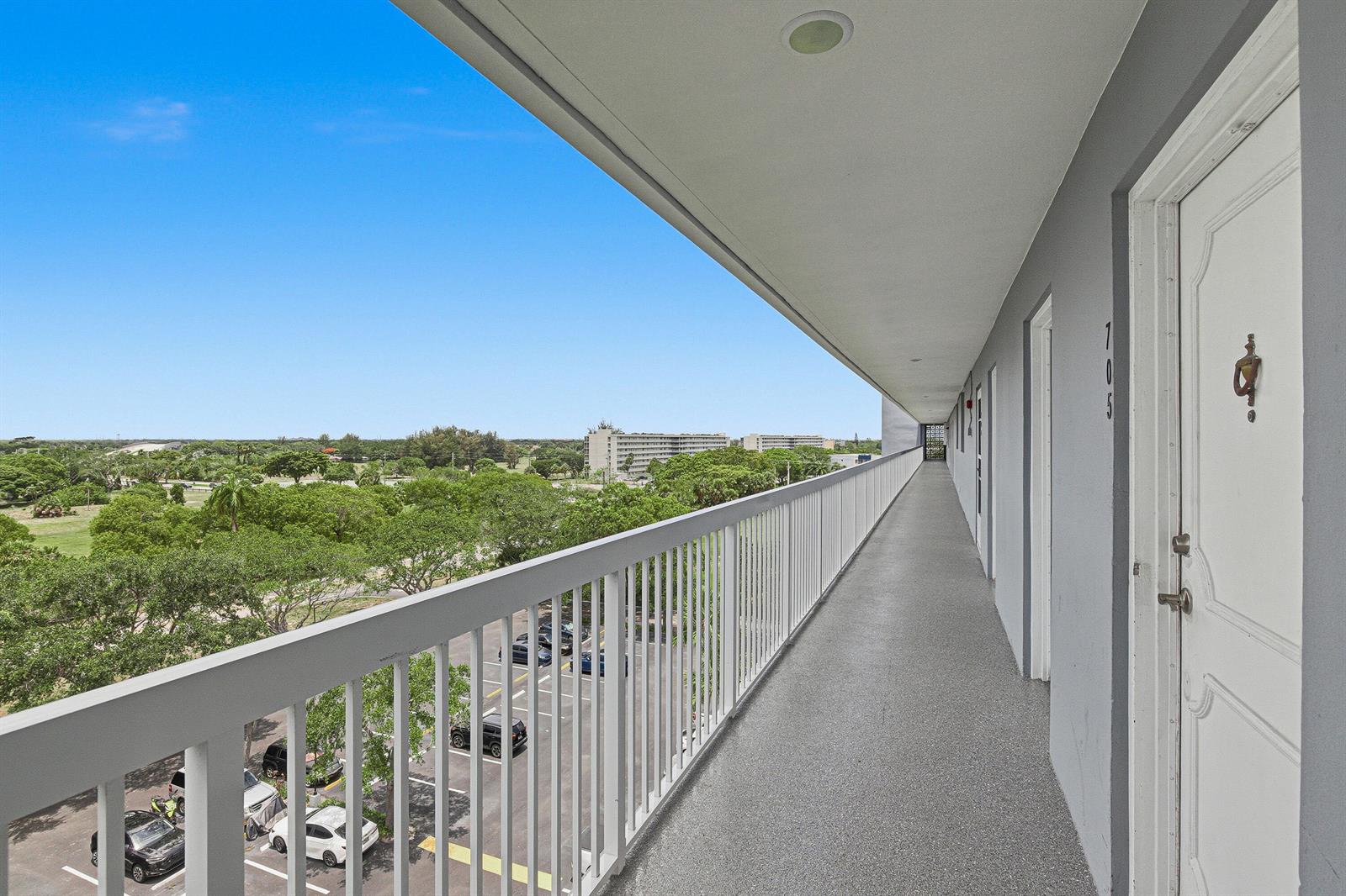 An outdoor apartment building walkway overlooks a parking lot and a green landscape — 5700 NW 2nd Avenue # 705, Boca Raton FL 33487, BOCA RATON, FL