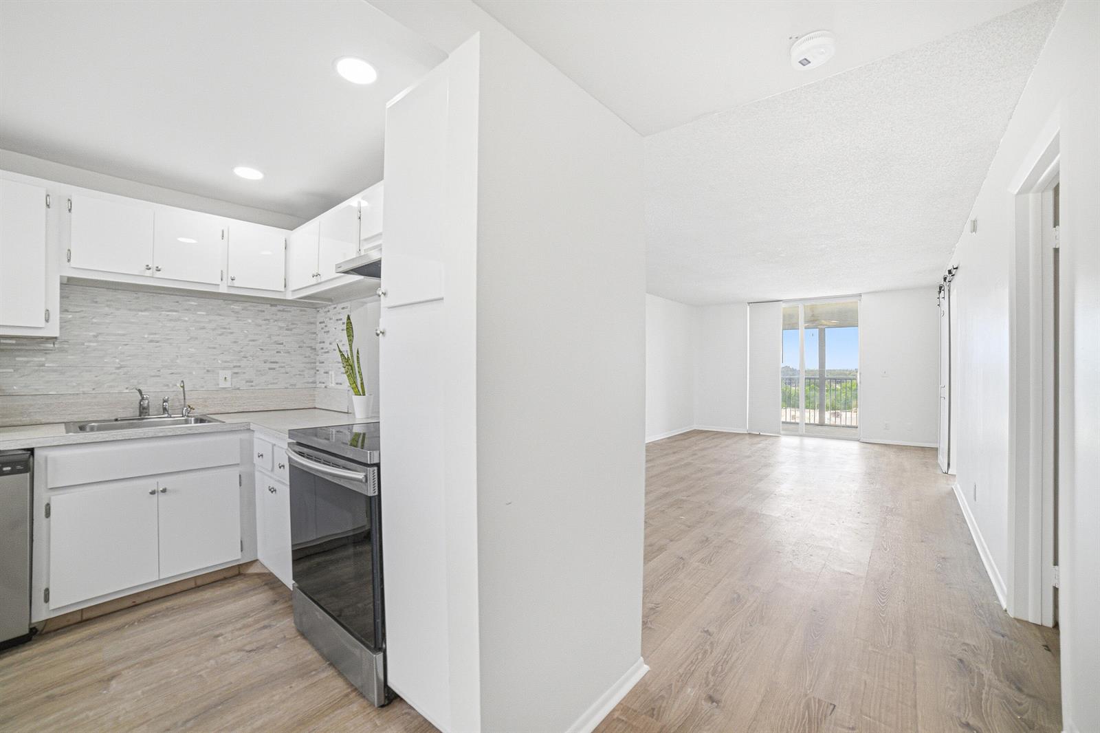 A kitchen with white cabinets and stainless steel appliances opens into a bright living area — 5700 NW 2nd Avenue # 705, Boca Raton FL 33487, BOCA RATON, FL