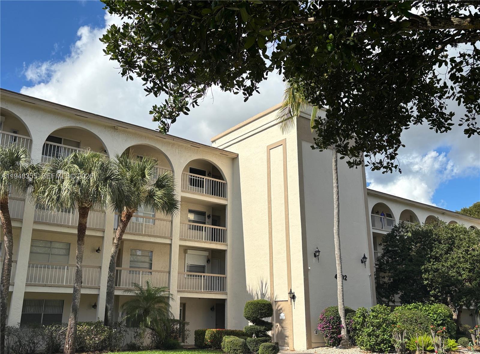 A multi-story apartment building features arched balconies and palm trees in front — 4602 Martinique Way # E3, Coconut Creek FL 33066, COCONUT CREEK, FL