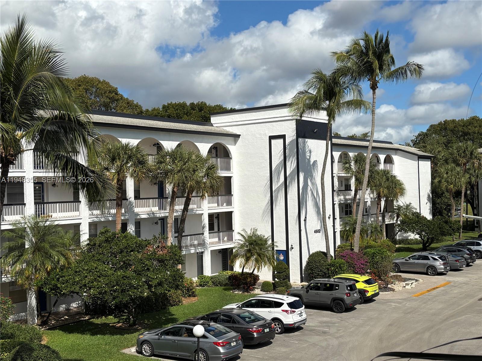 A three-story white apartment building with arched balconies and a parking lot in front — 4602 Martinique Way # E3, Coconut Creek FL 33066, COCONUT CREEK, FL