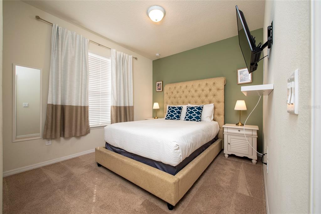 A bedroom features a tufted beige headboard, green accent wall, and a mounted television — 4611 TERRASONESTA DRIVE, DAVENPORT, FL