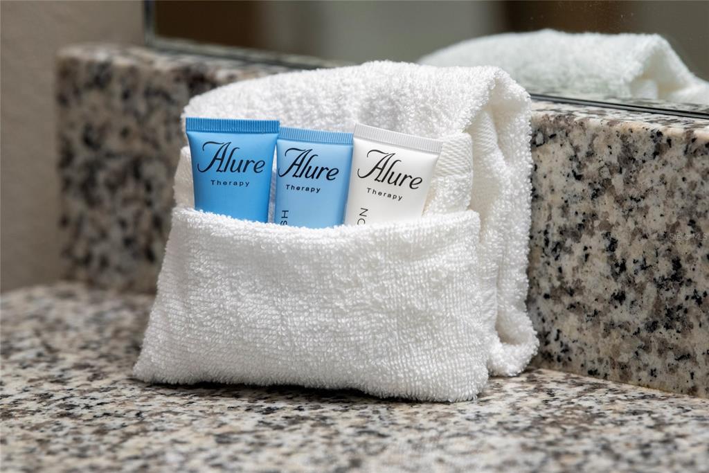 Three small Alure Therapy toiletry bottles are tucked into a folded white towel on a granite countertop — 4611 TERRASONESTA DRIVE, DAVENPORT, FL