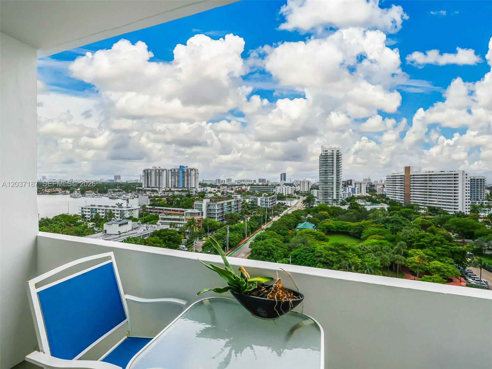 A balcony with a glass-topped table and blue chair overlooks a city park and skyline — 3 Island Ave # 14A, Miami Beach FL 33139, MIAMI BEACH, FL