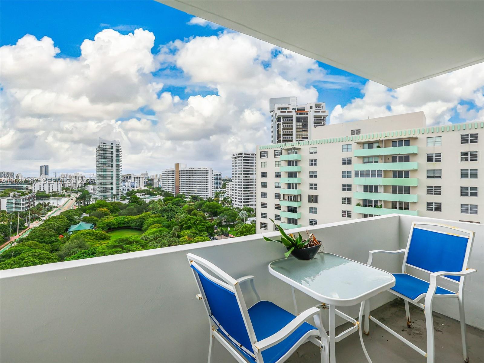 A balcony with a small glass table and two blue chairs overlooks a city skyline — 3 Island Ave # 14A, Miami Beach FL 33139, MIAMI BEACH, FL
