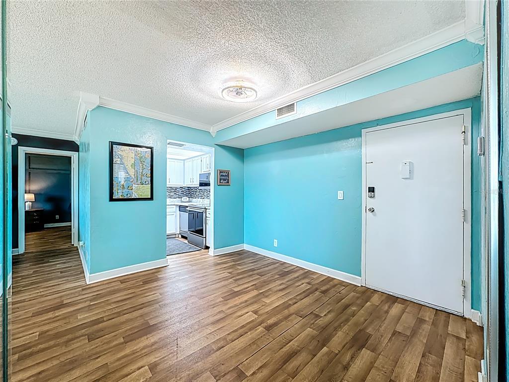 A bright blue room with wood-look flooring, a white entry door, and an adjacent kitchen — 2901 26TH STREET W UNIT 511, BRADENTON, FL
