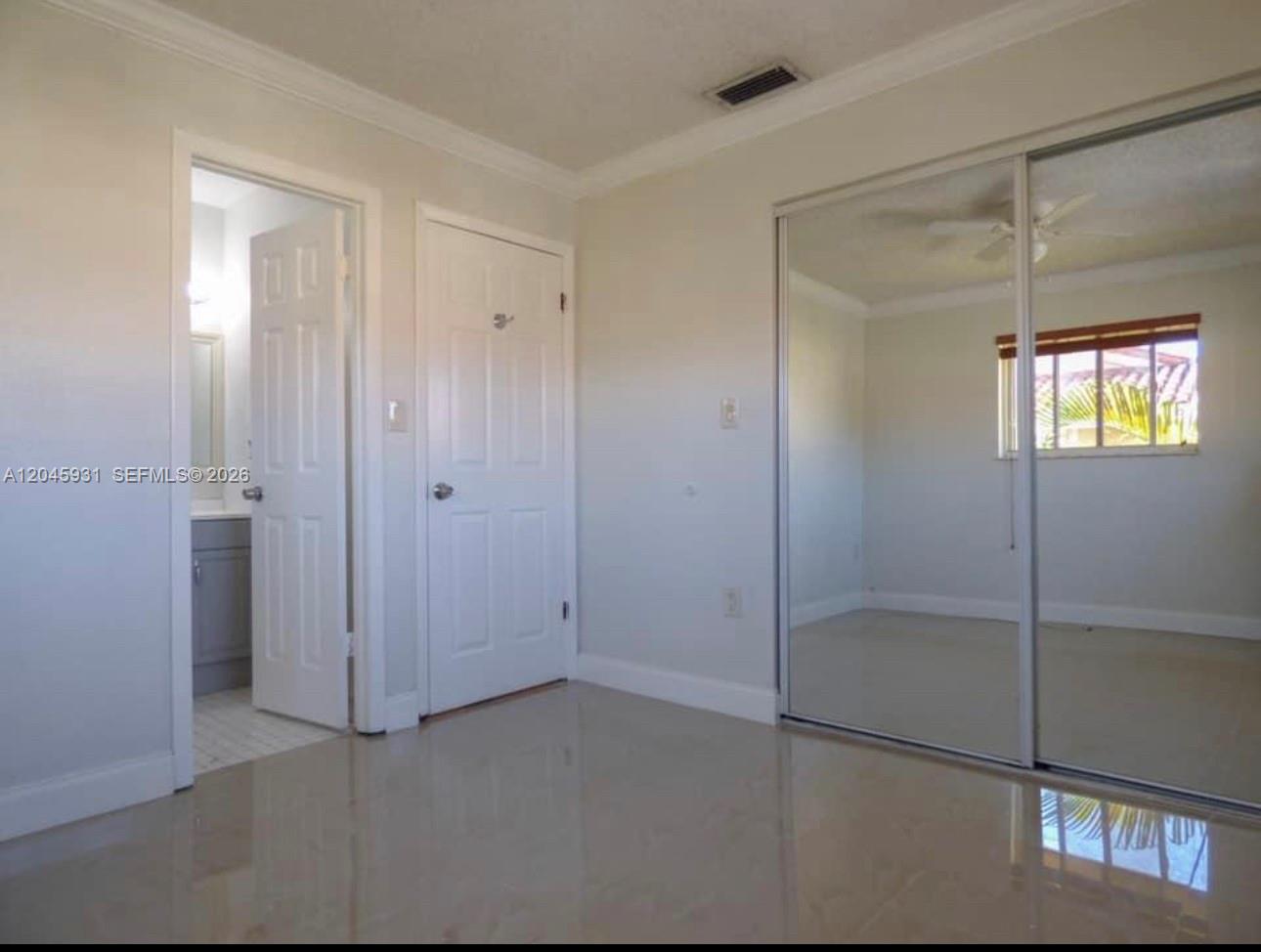 A bedroom with light-colored tile flooring, a mirrored closet, and an adjacent bathroom doorway — 8252 NW 6th Ter # 235, Miami FL 33126, MIAMI, FL