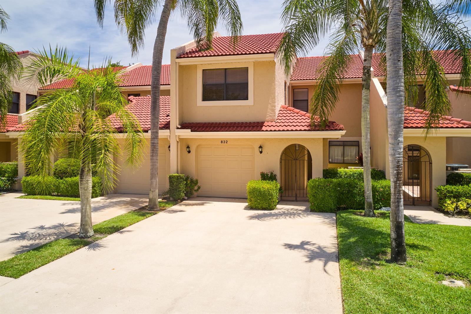 A two-story townhouse with a tan stucco exterior, red tile roof, and a single-car garage — 832 Windermere Way, Palm Beach Gardens FL 33418, PALM BEACH GARDENS, FL