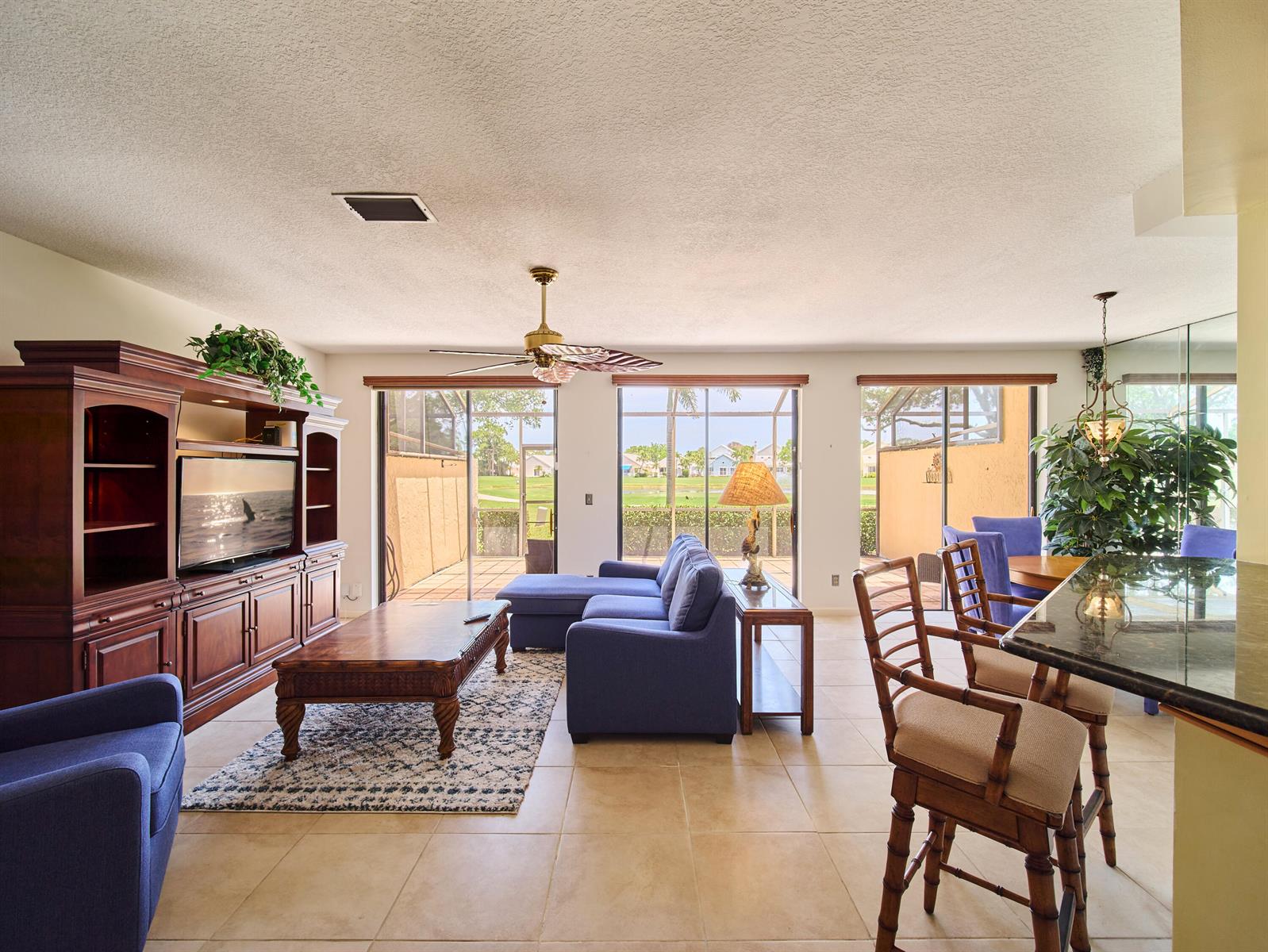 A living room with blue furniture, a wooden entertainment center, and sliding glass doors to a patio — 832 Windermere Way, Palm Beach Gardens FL 33418, PALM BEACH GARDENS, FL