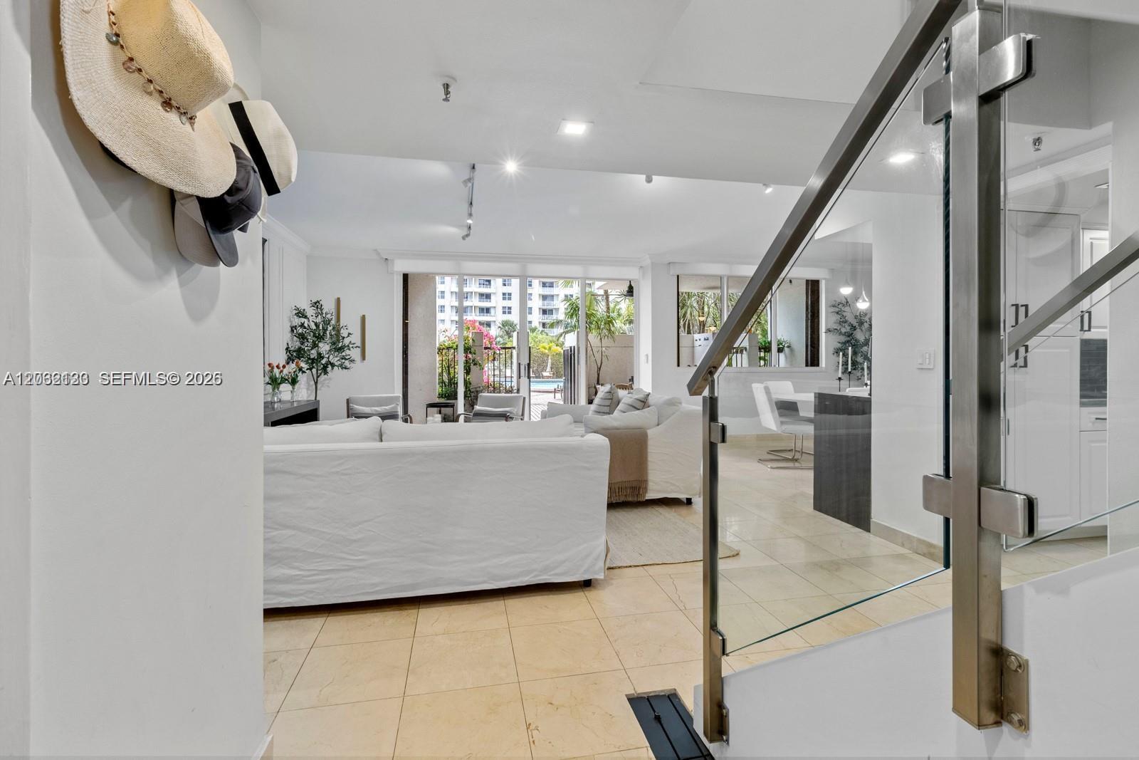 A bright living room features white sofas, tile flooring, and a glass-paneled staircase railing — 520 Brickell Key Dr # A307, Miami FL 33131, MIAMI, FL
