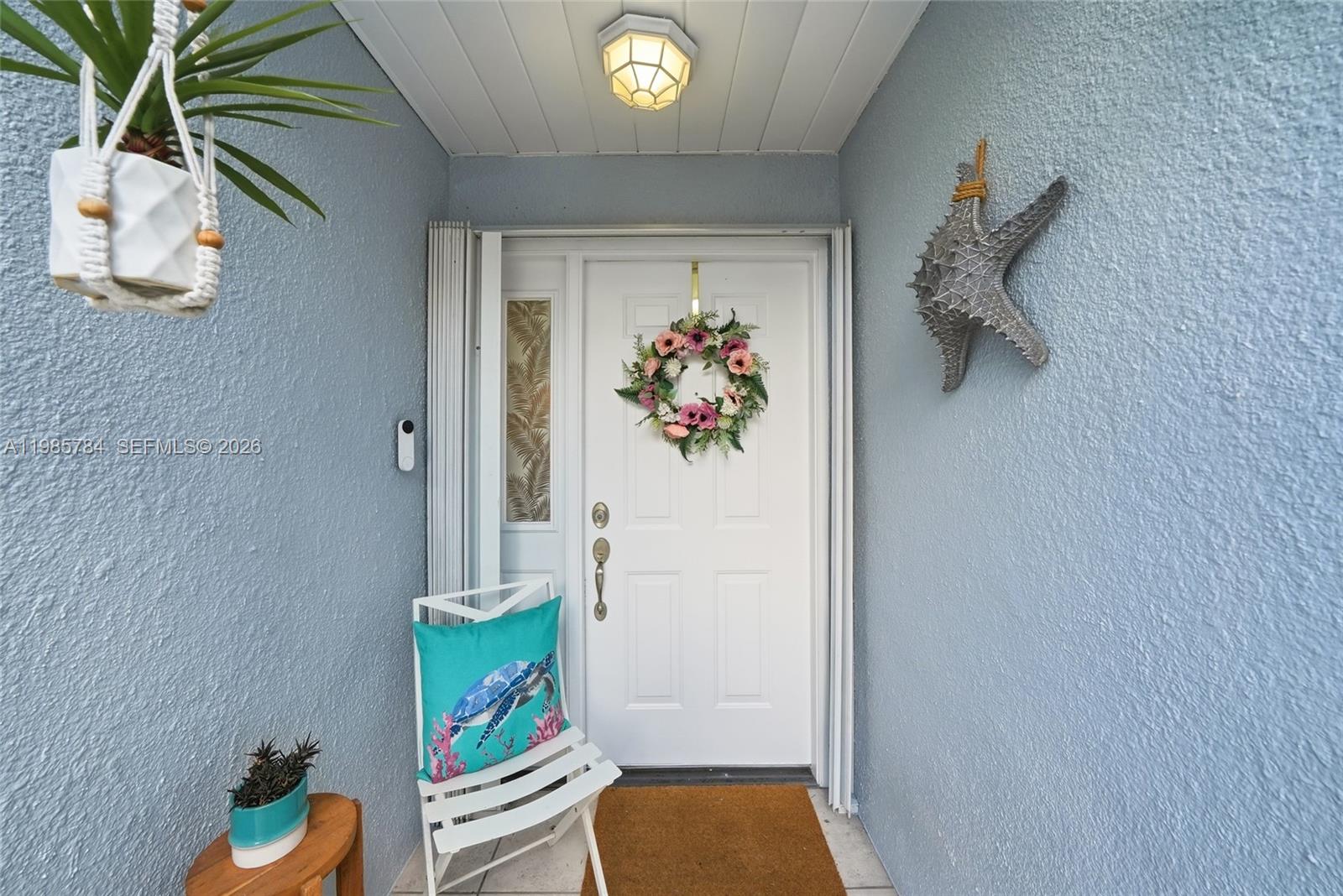 A white front door with a floral wreath is framed by light blue walls — 677 SE 22nd Dr, Homestead FL 33033, HOMESTEAD, FL
