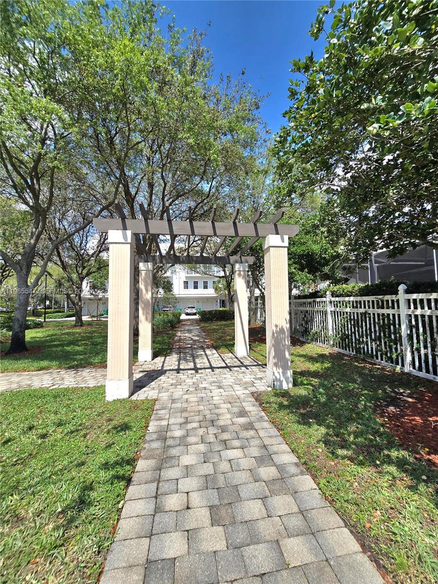 A stone walkway leads through a wooden pergola in a grassy outdoor area — 6841 N Lakeside Cir N # 1, Davie FL 33314, DAVIE, FL