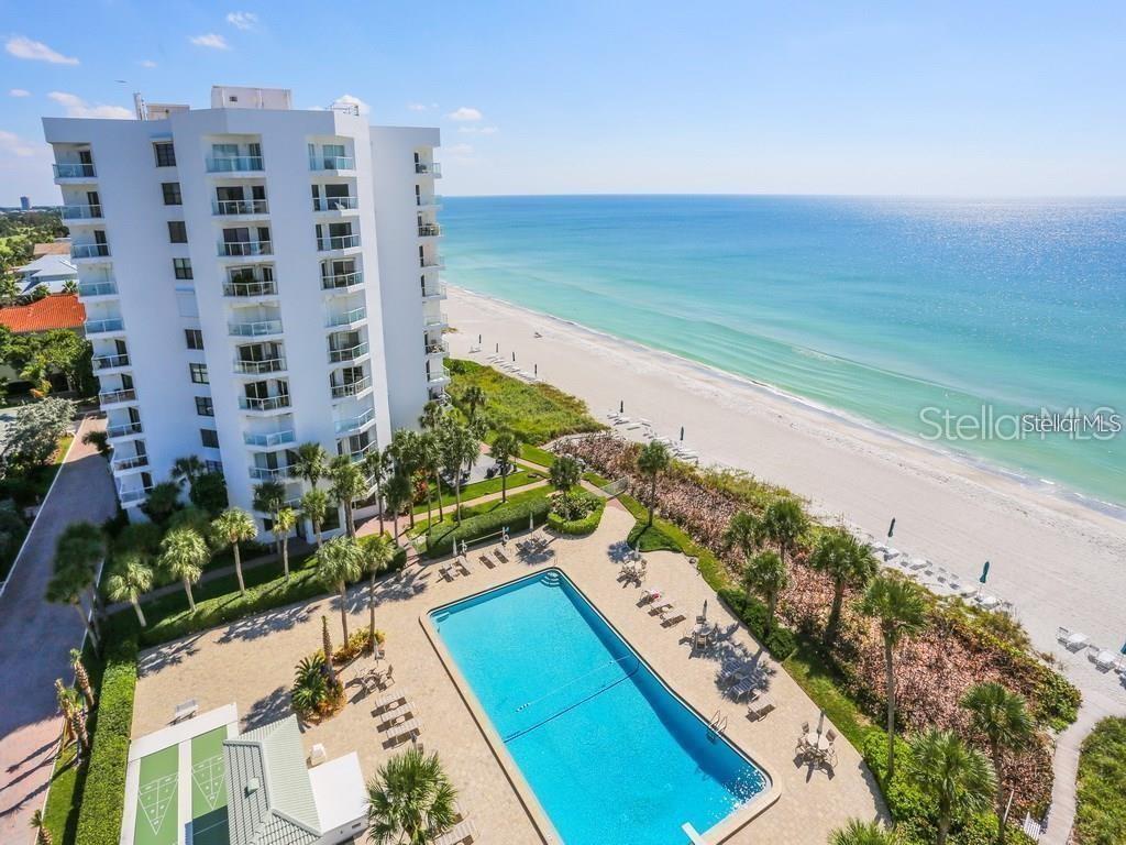 An aerial view shows a white high-rise condominium building next to a swimming pool and beach — 1050 LONGBOAT CLUB ROAD UNIT 1006, LONGBOAT KEY, FL