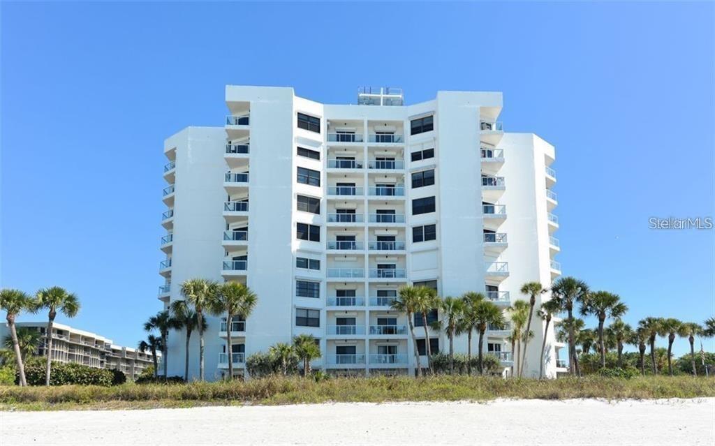 A white multi-story beachfront condominium building stands behind palm trees and a sandy beach — 1050 LONGBOAT CLUB ROAD UNIT 1006, LONGBOAT KEY, FL