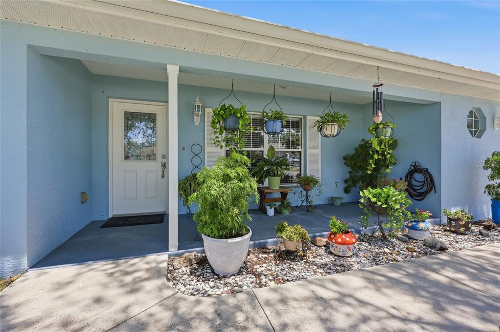 A light blue house exterior features a covered porch with hanging plants and potted greenery — 8708 SW 60TH CIRCLE, OCALA, FL
