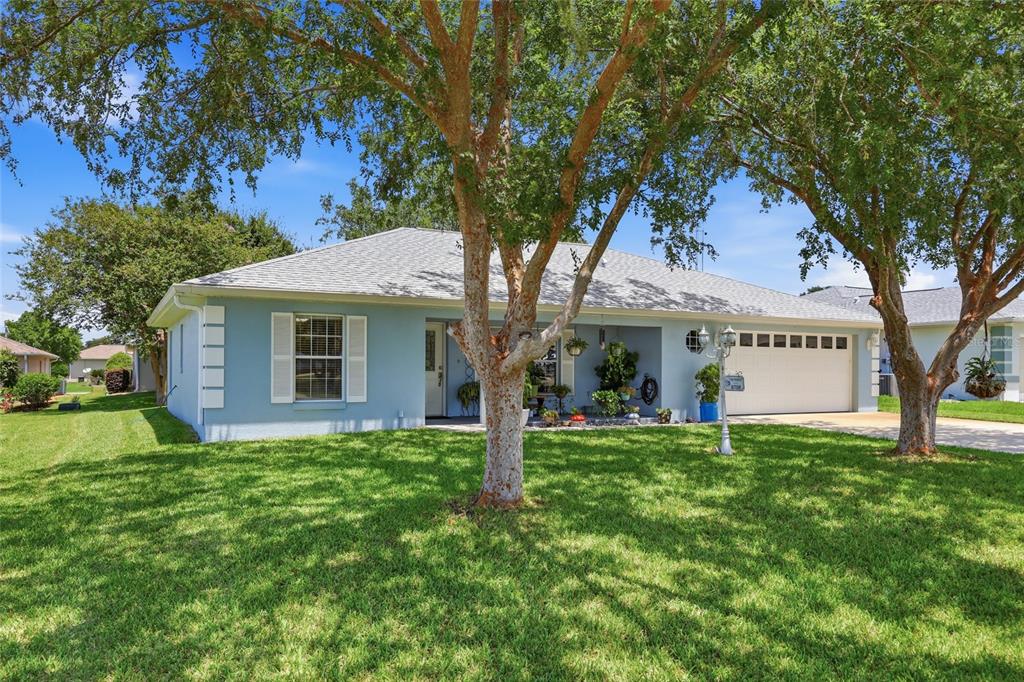 A light blue single-story house with a two-car garage and large trees in the yard — 8708 SW 60TH CIRCLE, OCALA, FL