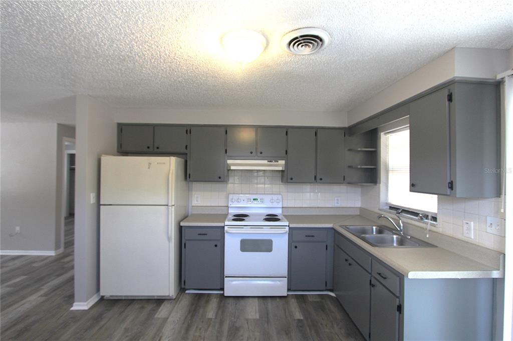 A kitchen features gray cabinets, white appliances, a tiled backsplash, and wood-look flooring — 5647 20TH STREET, ZEPHYRHILLS, FL