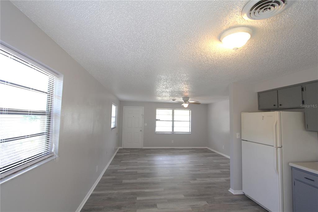 A living room with gray wood-look flooring, white walls, and a white refrigerator — 5647 20TH STREET, ZEPHYRHILLS, FL