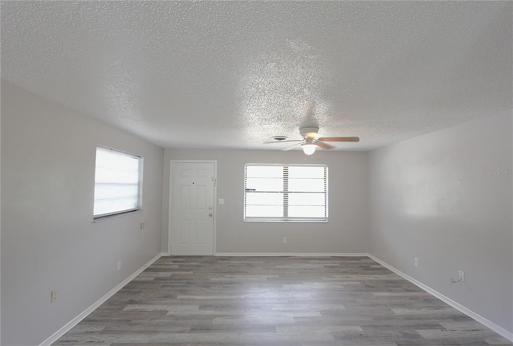 An empty room features light gray walls, wood-look flooring, a ceiling fan, and two windows — 5647 20TH STREET, ZEPHYRHILLS, FL