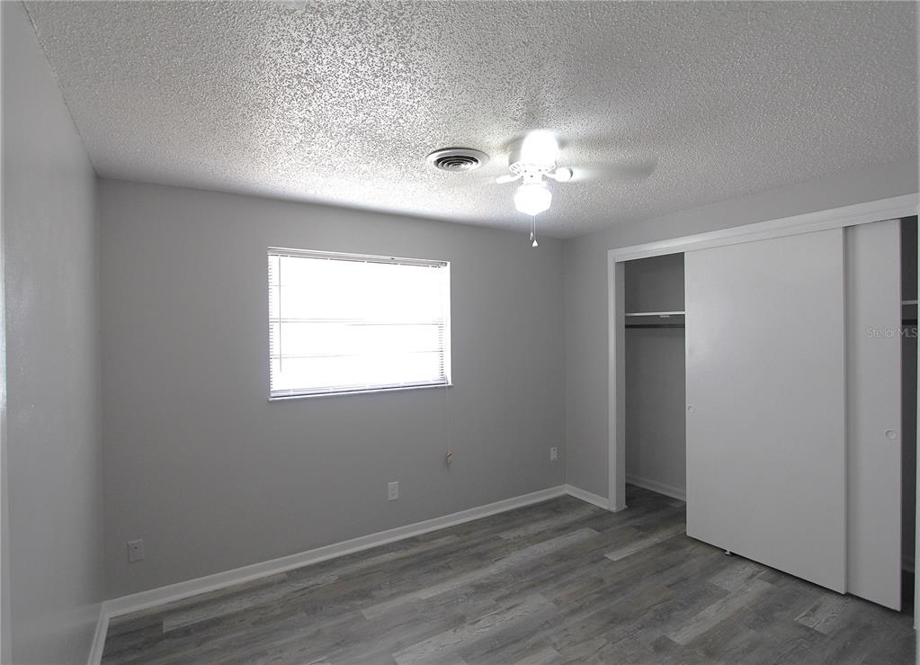 An empty bedroom features gray walls, wood-look flooring, a ceiling fan, and a sliding closet — 5647 20TH STREET, ZEPHYRHILLS, FL