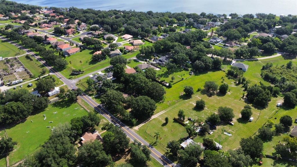 An aerial view shows a residential neighborhood with houses, trees, and a road near water — 11750 COUNTY ROAD 561, CLERMONT, FL