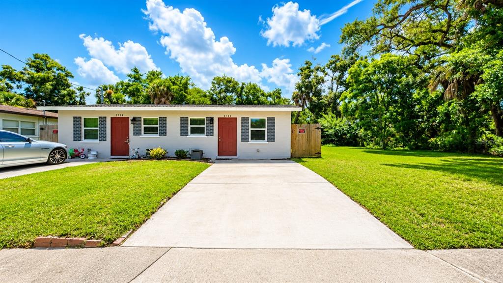A single-story duplex with a concrete driveway, two red doors, and a large grassy yard — 2728 GOODRICH AVENUE, SARASOTA, FL