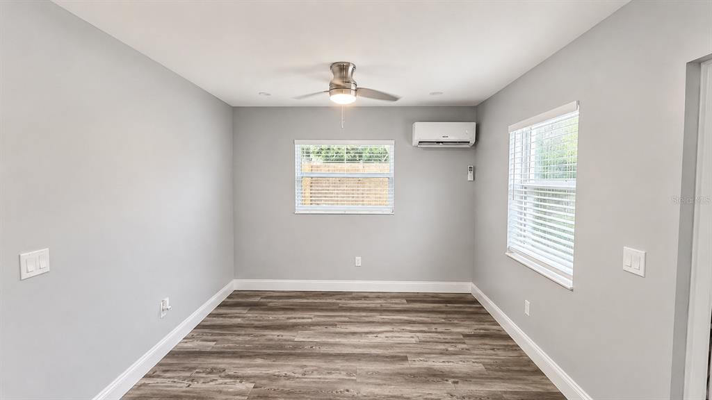 A bedroom with gray walls, wood-look flooring, a ceiling fan, and a wall-mounted air conditioner — 2728 GOODRICH AVENUE, SARASOTA, FL