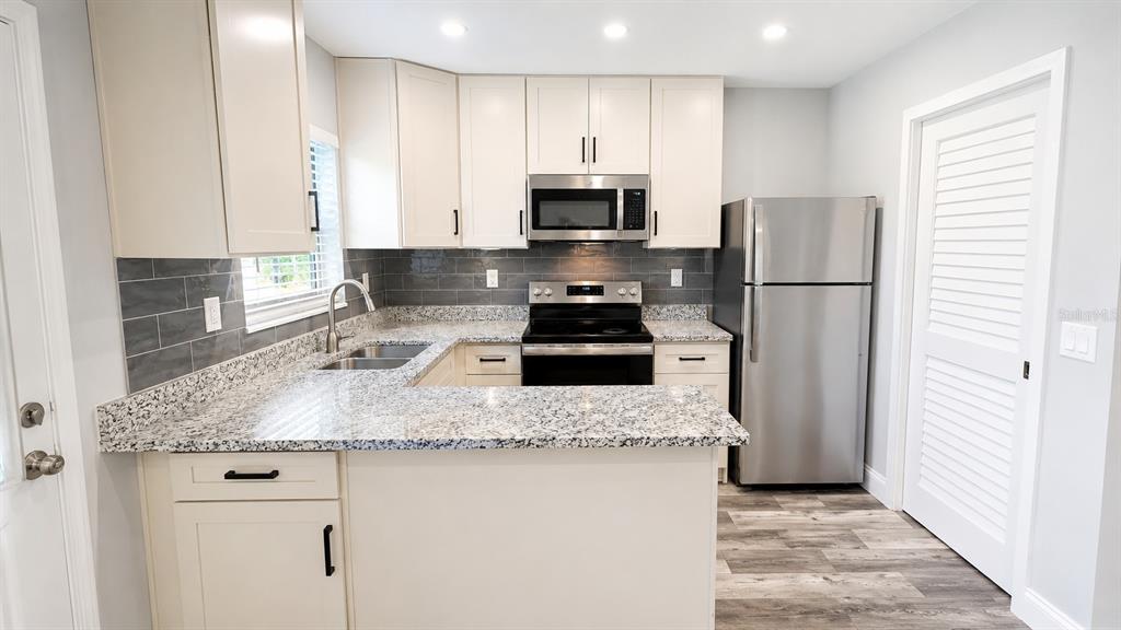 A kitchen features cream cabinets, granite countertops, stainless steel appliances, and a gray tiled backsplash — 2728 GOODRICH AVENUE, SARASOTA, FL