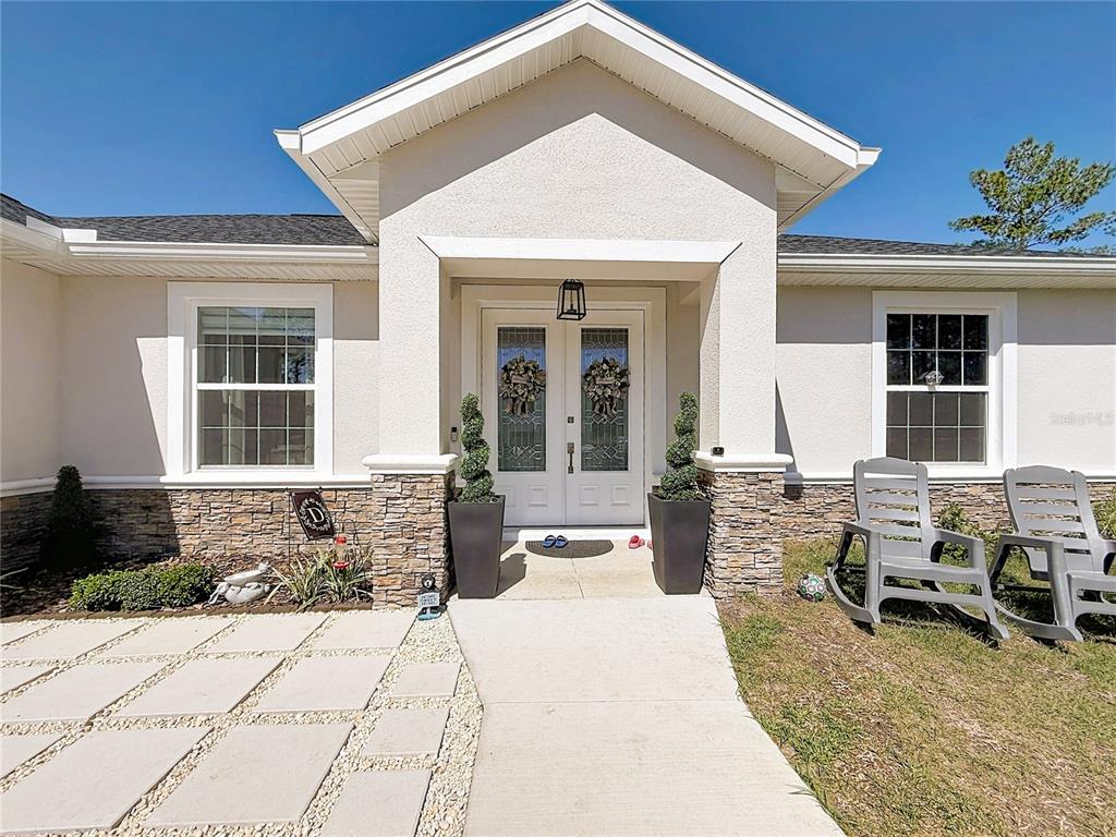 A front exterior view of a house featuring a stone-accented entryway and double glass doors — 8786 SW 127TH AVENUE, DUNNELLON, FL