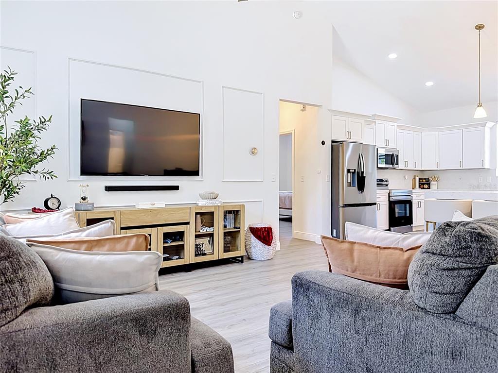 A living room with a wall-mounted television opens into a kitchen with white cabinetry — 8786 SW 127TH AVENUE, DUNNELLON, FL