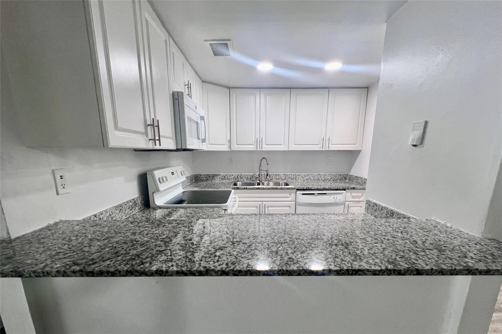 A kitchen features white cabinets, granite countertops, and stainless steel appliances — 17350 NW 68th Avenue # 419, Hialeah FL 33015, HIALEAH, FL