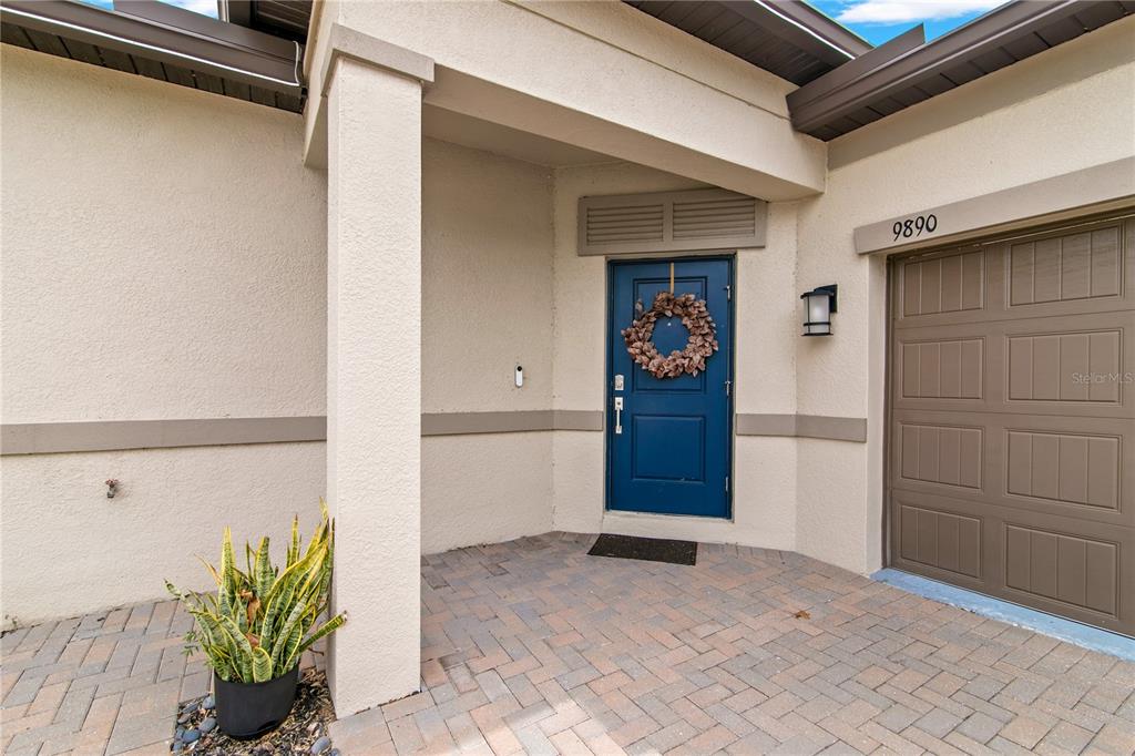 A blue front door with a wreath sits next to a garage on a patio — 9890 RED BAY LOOP, LAND O LAKES, FL