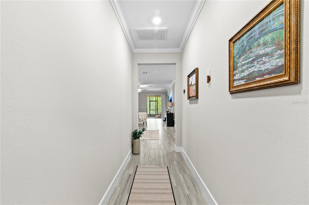 A hallway with light-colored walls and wood-look tile flooring leads toward an open living area — 9890 RED BAY LOOP, LAND O LAKES, FL