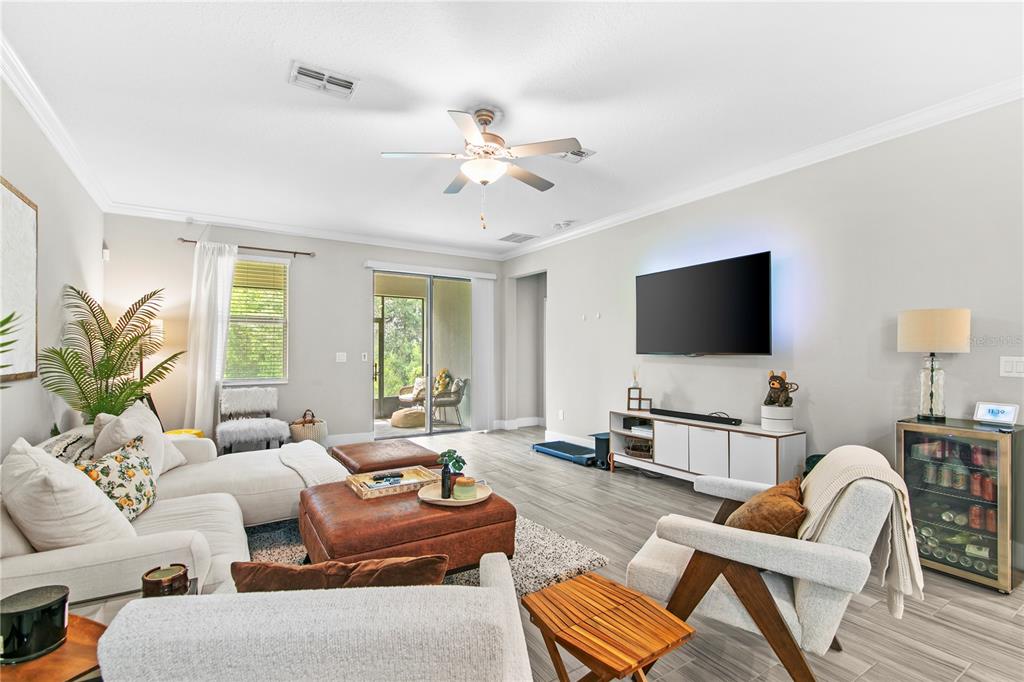 A living room features a sectional sofa, leather ottoman, television, and sliding glass patio doors — 9890 RED BAY LOOP, LAND O LAKES, FL