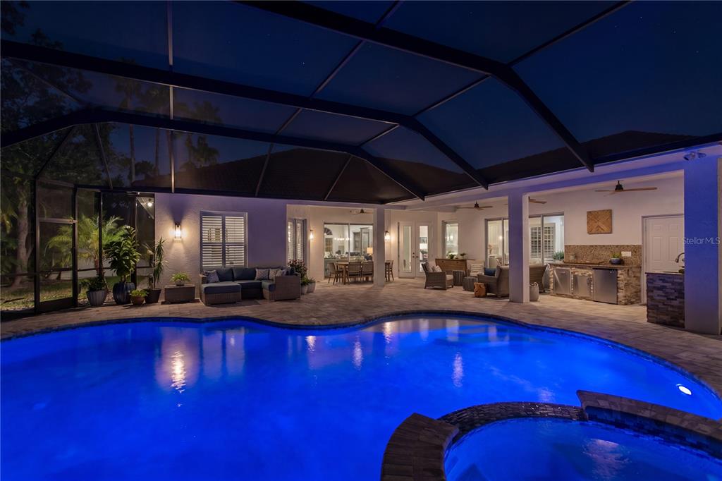 A covered patio with a swimming pool, hot tub, and outdoor kitchen at night — 2801 SHORE BREEZE DRIVE, TAMPA, FL