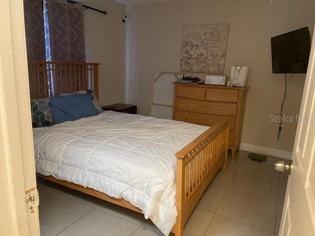 A bedroom features a wooden bed frame, a matching dresser, and light-colored tile flooring — 12220 CORAL REEF DRIVE, ORLANDO, FL