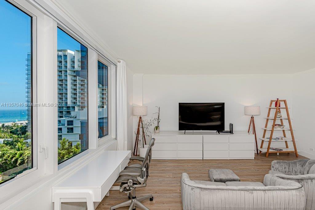 A bright living room features a desk by floor-to-ceiling windows overlooking the ocean — 2301 Collins Ave # 842, Miami Beach FL 33139, MIAMI BEACH, FL