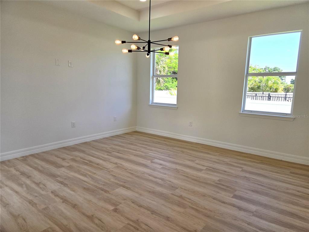 An empty room features light wood-look flooring, white walls, two windows, and a modern chandelier — 3382 EVERETT TERRACE, NORTH PORT, FL