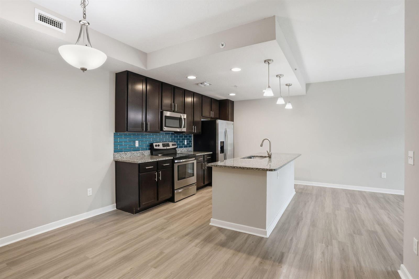 A kitchen features dark wood cabinets, granite countertops, a blue tile backsplash, and an island — 3601 High Ridge Road # 206, Boynton Beach FL 33426, BOYNTON BEACH, FL