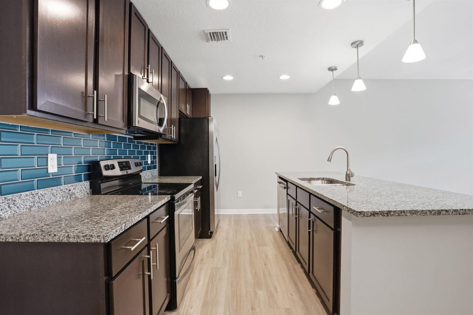 A kitchen features dark wood cabinets, granite countertops, a blue subway tile backsplash, and appliances — 3601 High Ridge Road # 206, Boynton Beach FL 33426, BOYNTON BEACH, FL