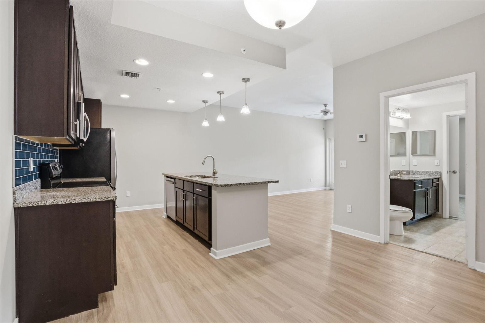 A kitchen with dark cabinets, granite countertops, and a center island opens to a living area — 3601 High Ridge Road # 206, Boynton Beach FL 33426, BOYNTON BEACH, FL