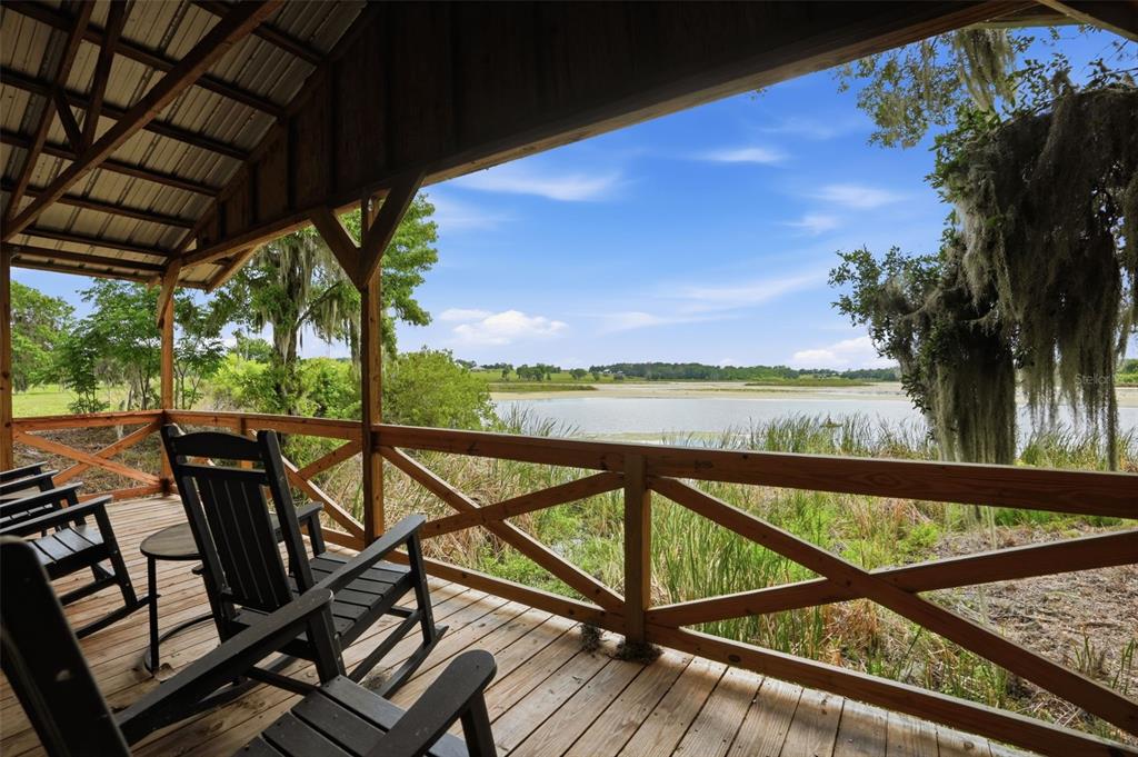 A wooden porch with rocking chairs overlooks a lake surrounded by trees and tall grass — 18610 TOWNSEND HOUSE ROAD, DADE CITY, FL