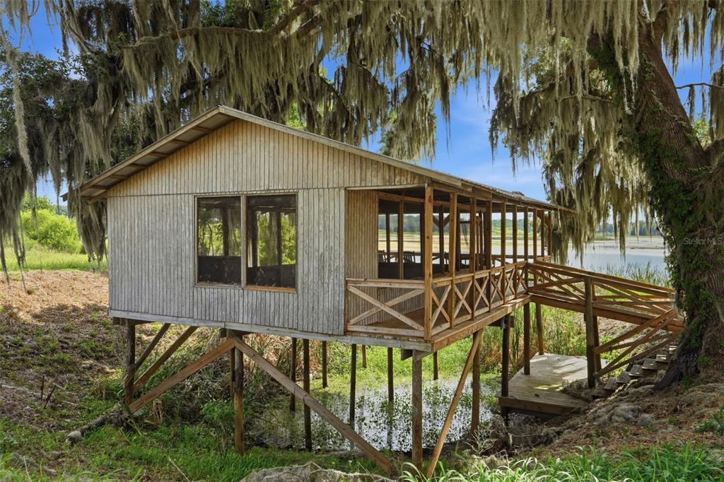 A rustic wooden cabin on stilts features a screened porch overlooking a marshy landscape — 18610 TOWNSEND HOUSE ROAD, DADE CITY, FL