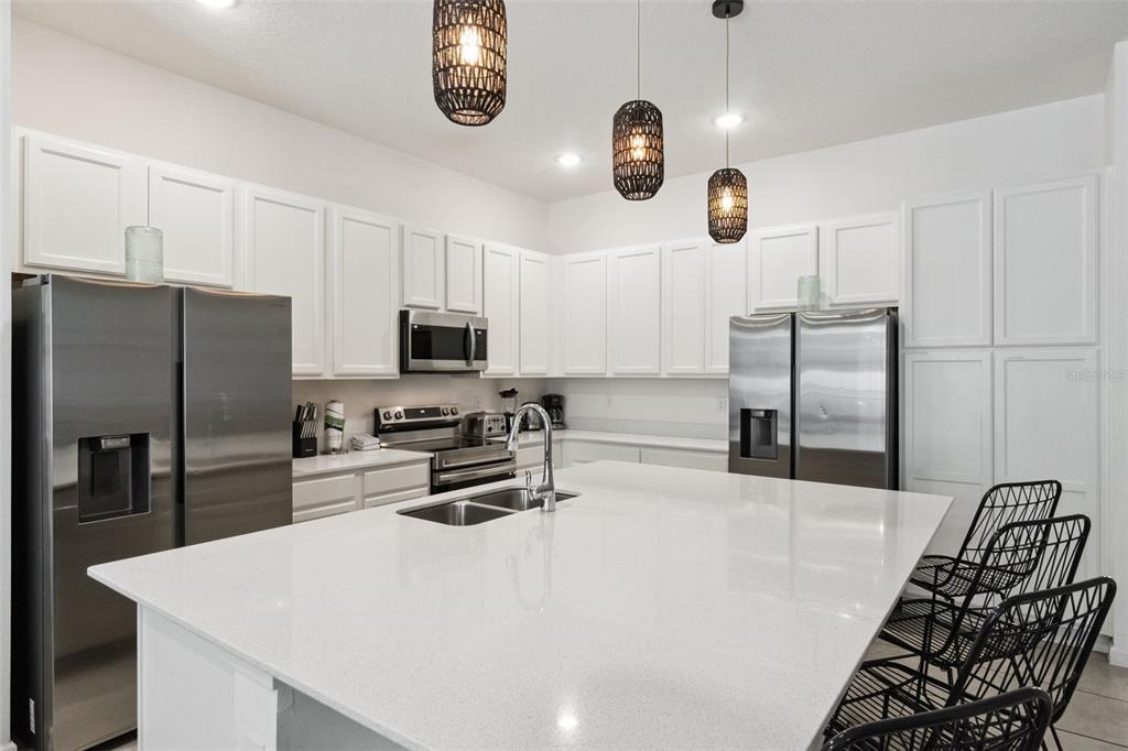 A modern kitchen features white cabinetry, stainless steel appliances, a large quartz island, and pendant lighting — 262 MARCELLO BOULEVARD, KISSIMMEE, FL