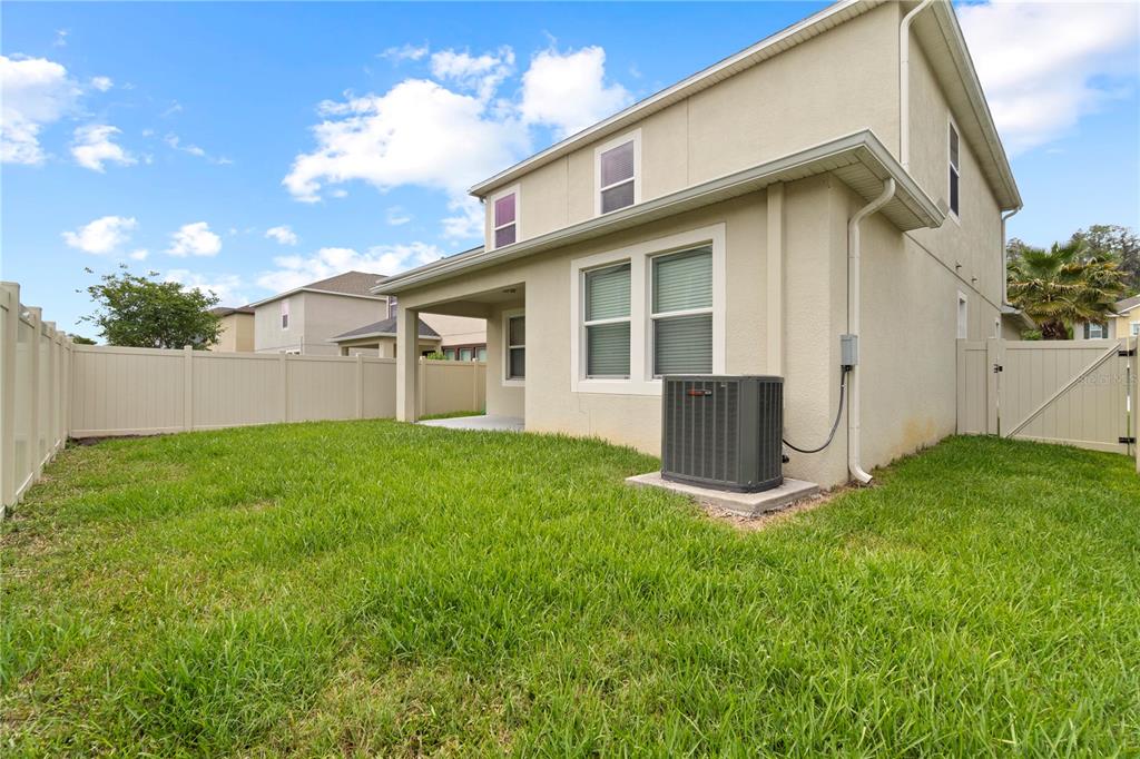 The backyard of a two-story house features a covered patio, lawn, and vinyl fencing — 1588 LUDINGTON AVENUE, WESLEY CHAPEL, FL