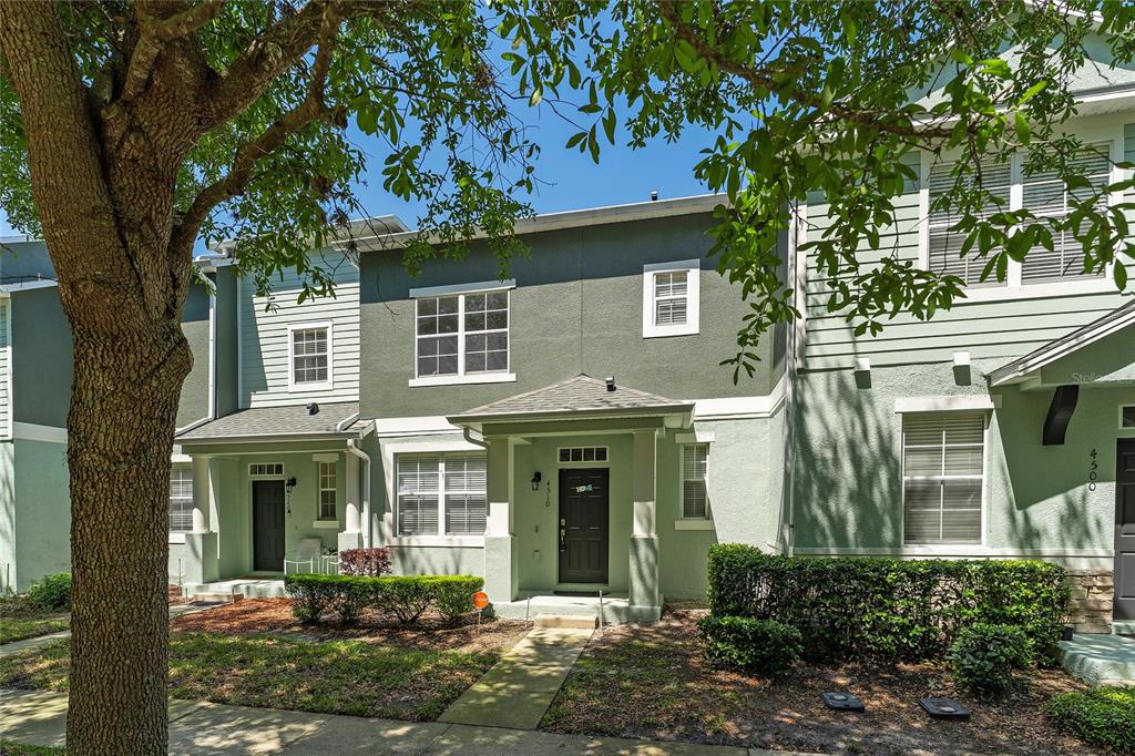 A multi-story townhouse exterior with a green facade, covered entryway, and a large tree — 4510 CAPITAL BOULEVARD, ST CLOUD, FL