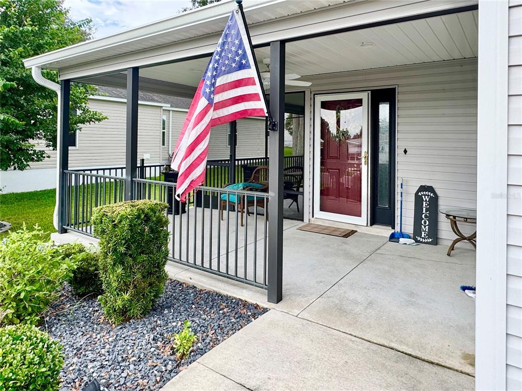 A covered front porch features a red door, an American flag, and a welcome sign — 810 ROSEAPPLE AVENUE, LADY LAKE, FL