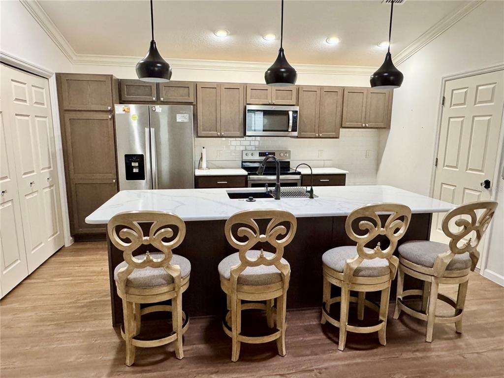 A kitchen features a white island with four chairs, stainless steel appliances, and brown cabinetry — 810 ROSEAPPLE AVENUE, LADY LAKE, FL