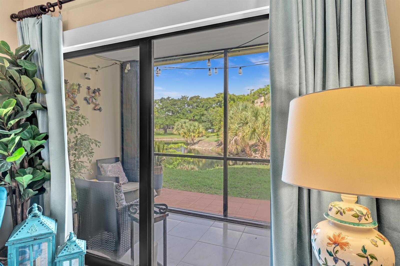 A view through a sliding glass door shows a screened patio overlooking a pond — 912 SW 9th Street Circle # 105, Boca Raton FL 33486, BOCA RATON, FL